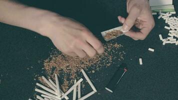Man in Black Clothing is Rolling a Hand Made Cigarette Using Papers, Filters and Tobacco. A Way to Save on Tobacco Products. Tobacco Product Economy Concept. Top View video