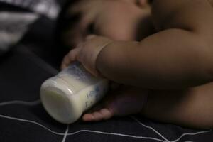 Baby with bottle lying in comfortable bed. Baby Drinks Milk From Bottle. photo