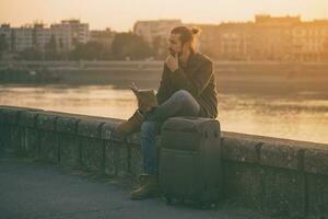 Confused businessman with suitcase and city map sitting lost by the river.Toned image photo