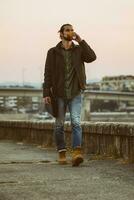 Handsome modern businessman with laptop bag drinking coffee and walking by the river.Toned image photo