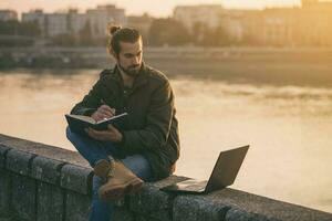 Handsome businessman using personal organizer and laptop while sitting by the river.Tone image photo
