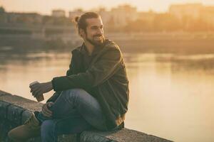 Handsome modern businessman enjoys drinking coffee and resting by the river.Toned image photo