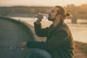 Handsome modern businessman enjoys drinking water and resting by the river.Toned image photo