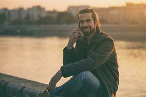 Handsome modern businessman using phone while sitting by the river.Toned image. photo