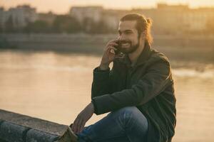 Handsome modern businessman using phone while sitting by the river.Toned image. photo