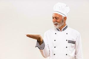 Portrait of senior chef with empty plate on gray background. photo