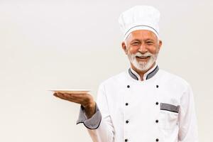 Portrait of senior chef with empty plate on gray background. photo