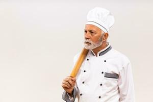 Image of angry senior chef holding rolling pin on gray background. photo