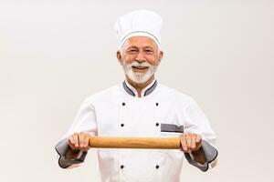 Portrait of senior chef holding rolling pin on gray background. photo