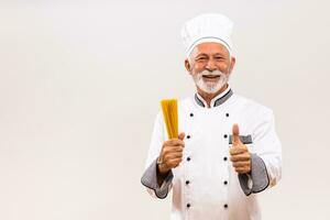 Portrait of senior chef holding spaghetti and showing thumb up  on gray background. photo