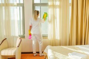 Image of hotel maid cleaning windows in a room. photo