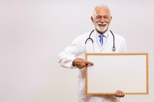 Portrait of senior doctor holding white board on  gray background. photo