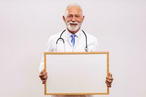 Portrait of senior doctor holding whiteboard on  gray background. photo