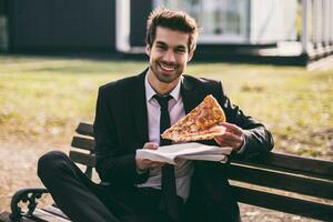 Elegant businessman enjoys eating pizza on his lunch break while sitting outdoor.Toned image. photo