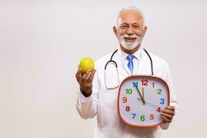 retrato de mayor médico participación manzana y reloj en gris antecedentes. foto