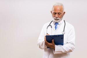 Portrait of  senior doctor writing notes  on  gray background. photo