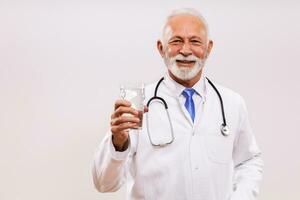 Portrait of  senior doctor holding glass of water on gray background. photo