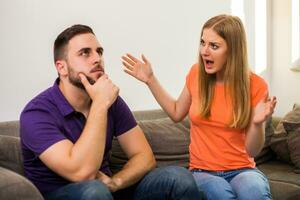 enojado esposa y marido son teniendo conflicto mientras ellos sentado en sofá a su hogar. foto