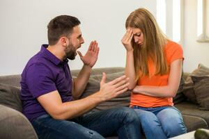 Angry wife and husband are having conflict while they sitting on sofa at their home. photo