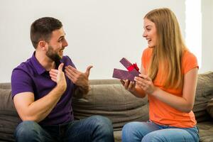 Wife giving present to her husband while they sitting on sofa at their home. photo