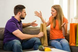 Couple having conflict because wife spent too much money on shopping while they sitting at sofa in their home. photo