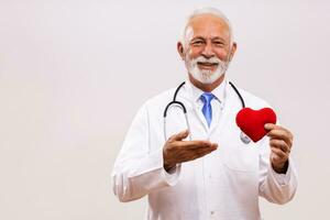 Portrait of senior doctor with stethoscope showing heart shape on gray background. photo