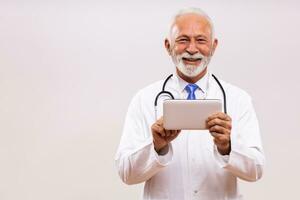 Portrait of senior doctor using digital tablet on gray background. photo