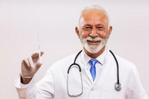 Portrait of senior doctor holding injection on gray background. photo