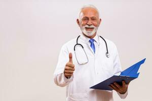 Portrait of senior doctor showing thumb up and holding documents on gray background. photo