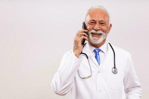 retrato de mayor médico hablando en el teléfono en gris antecedentes. foto