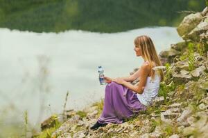 Woman enjoys drinking water while spending time by the lake. photo