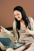 Young woman using laptop and showing thubs up photo