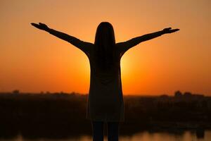 Silhouette of a woman with arms outstretched at the sunset. photo