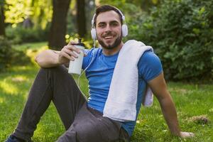 Handsome man with headphones  drinking water and resting after exercise in the park. photo