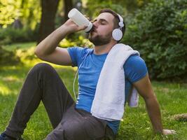 Handsome man with headphones  drinking water and resting after exercise in the park. photo