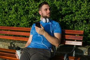 Handsome man using phone and drinking water while resting after exercise. photo