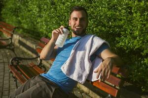 hermoso hombre Bebiendo agua y descansando después ejercicio en el parque. foto