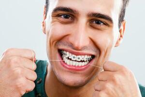 Man with braces cleaning his teeth with dental floss photo