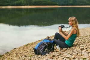 mujer caminante utilizando prismáticos mientras sentado por el lago. foto