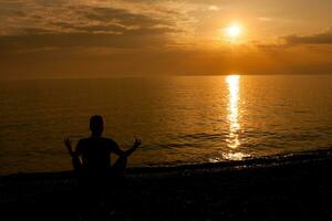 Silhouette of a man meditating on the beach at sunset photo