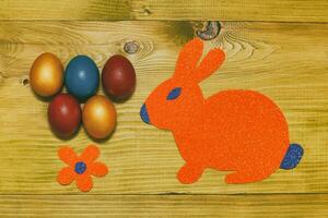 Painted Easter eggs with paper bunny and flower on wooden table.Toned photo. photo
