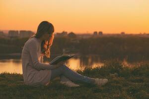 Woman enjoys reading a book with a sunset over the city. photo