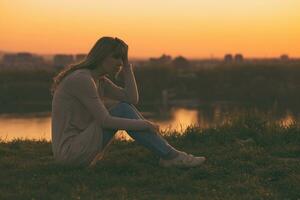 triste mujer sentado a el puesta de sol y pensamiento. foto