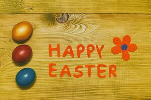 Happy Easter message with painted  eggs  and flower on wooden table.Toned photo. photo