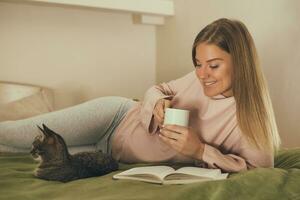 Beautiful woman reading book,drinking coffee and spending time with her cat.Toned image. photo