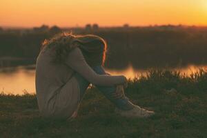 triste mujer sentado a el puesta de sol. foto