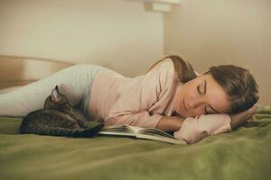 Beautiful woman fall asleep with her cat while reading a book.Toned image. photo