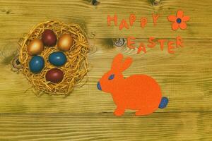Happy Easter message with painted eggs in straw,bunny and flower on wooden table.Toned photo. photo
