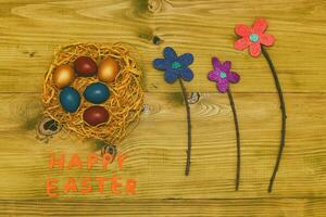 Happy Easter message with painted  eggs in straw  and flowers on wooden table.Toned photo. photo