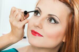 Make up artist applying mascara on a beautiful woman photo